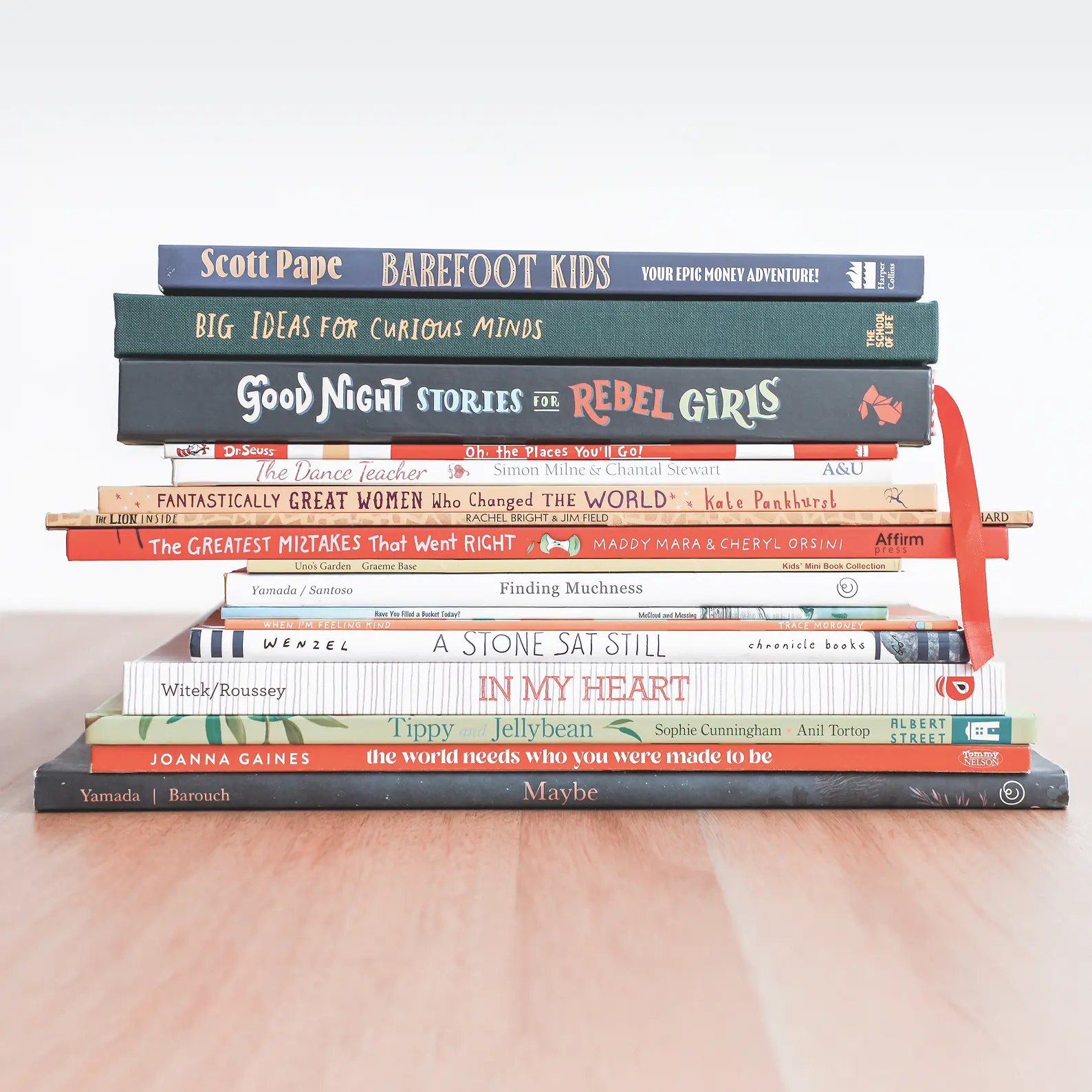 Stack of various children's books on wooden floor.